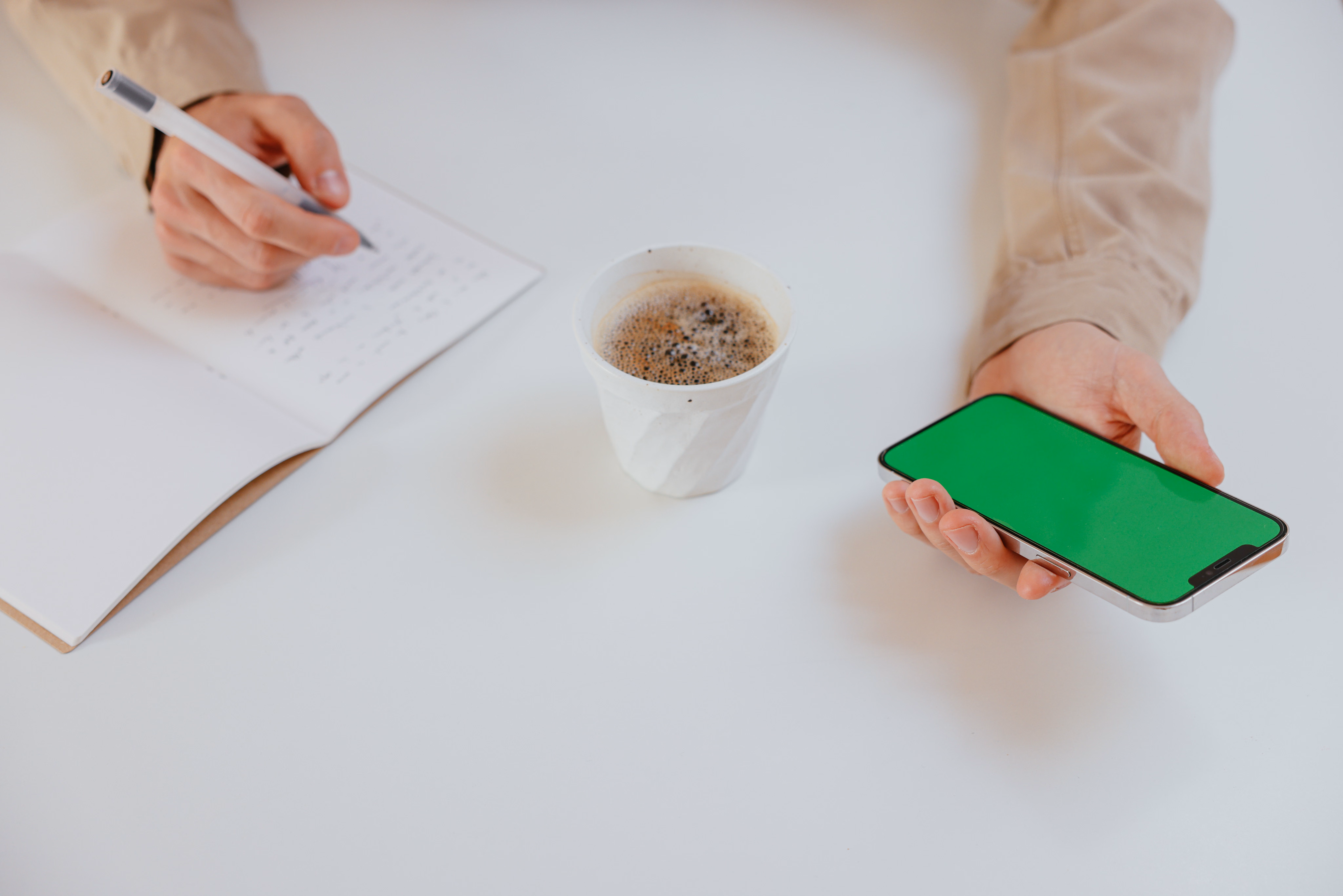 Person writing notes on a smartphone with a cup of coffee