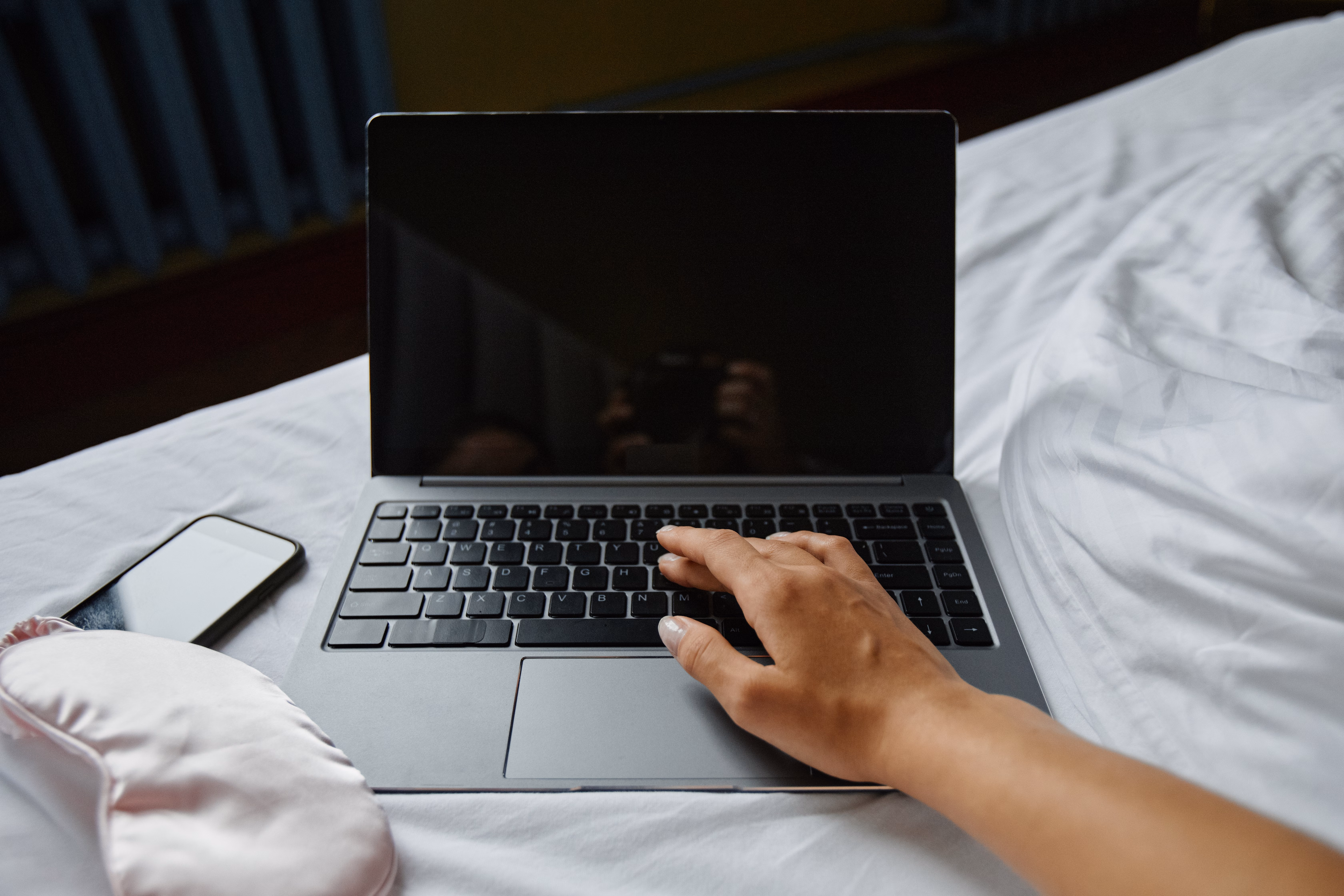 Laptop and eye mask resting on a bed at night
